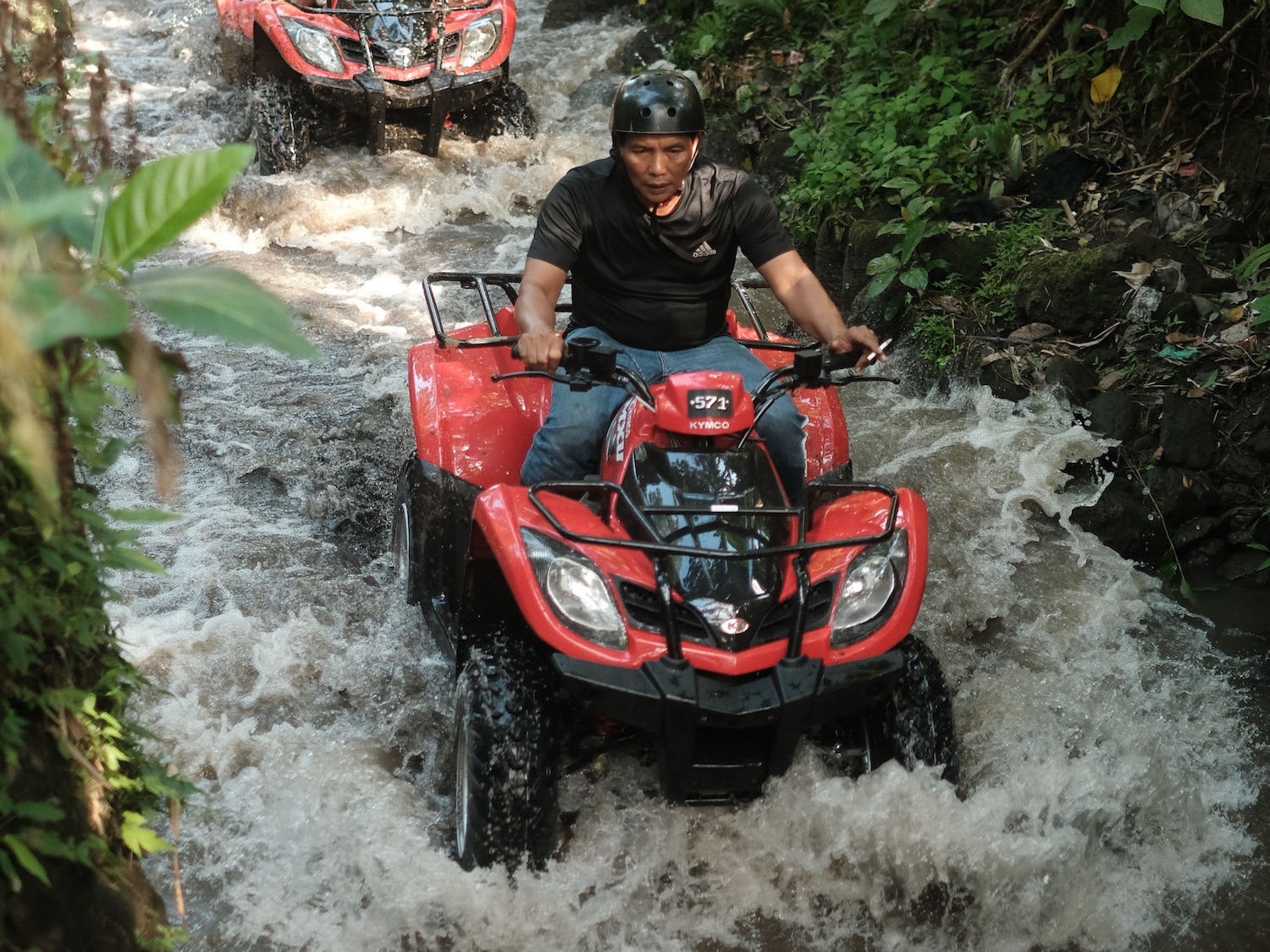 Rider driving a single ATV quad bike through the river track in Ubud