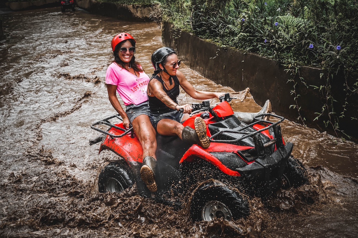 Two riders sharing a tandem ATV quad bike splashing through the muddy river in Ubud